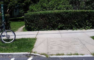 Curb ramp for the Old Croton Aqueduct leading to a hedge row, blocking direct access to/from the OCA