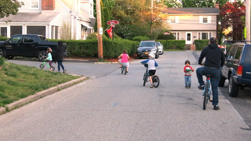 Small children cycling and walking on a small residential street.