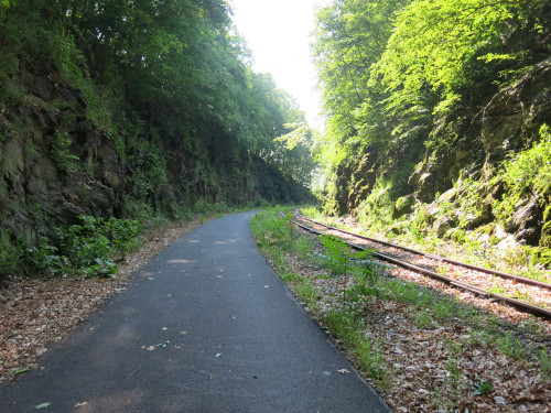 Photo of a paved, shady trail in a rock cut, curving to the right.