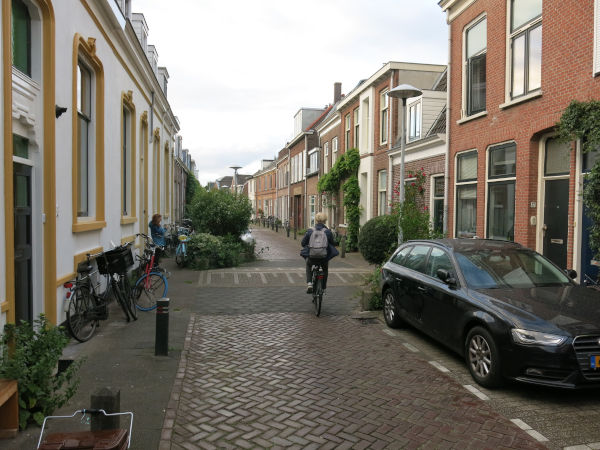 Photo of a narrow, traffic calmed street. 2.5 story buildings on each side. Cars are parked on the right side near us, then there's a speed hump and the parking shifts to the other side of the street.