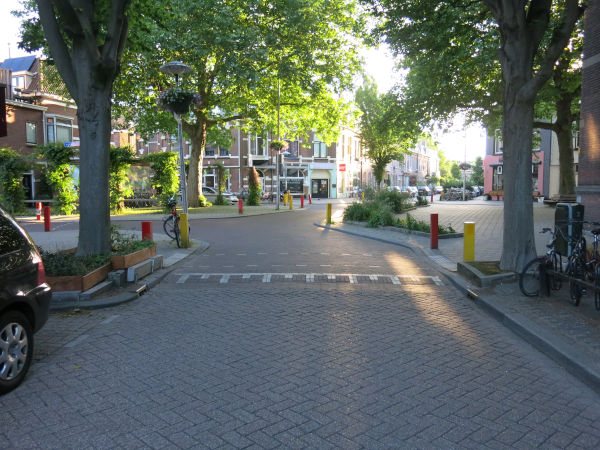 Photo of a traffic calmed intersection. Curb extensions and bollards keep people driving at safe speeds. Trees and sidewalks abound.