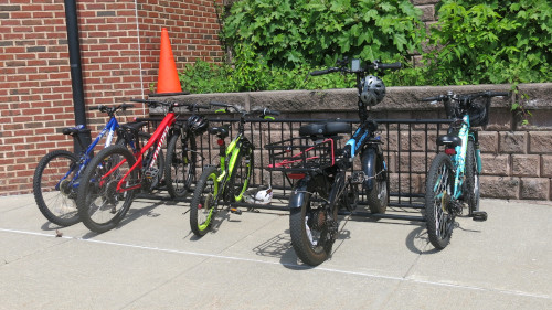 Photo of several bikes parked in a bike rack in front of a brick wall.