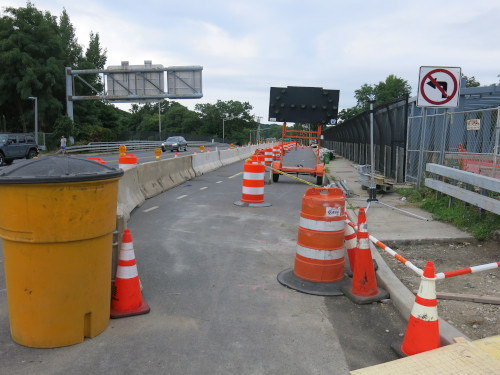 A temporary walkway through a constuction zone. Jersey barriers on the left. Barrels on the right.