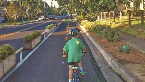 Photo of a kid cycling along a 2-way protected mobility lane in a suburban area.