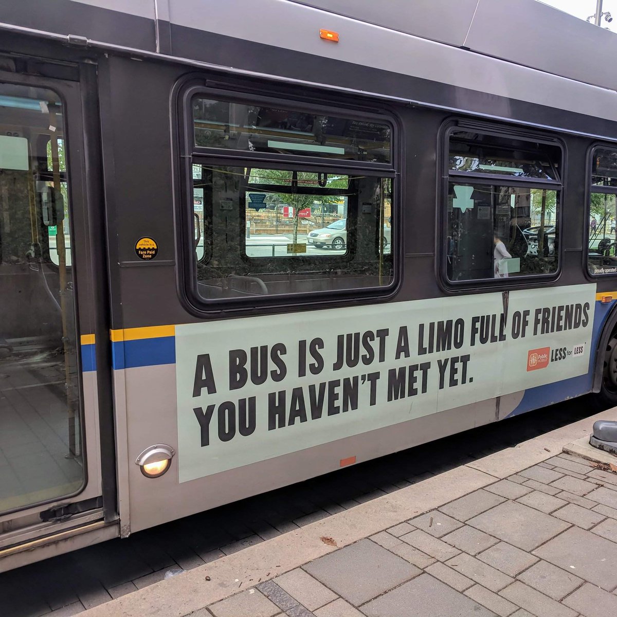 Photo of a city bus with a poster on the side saying A bus is just a limo full of friends you haven't met yet.