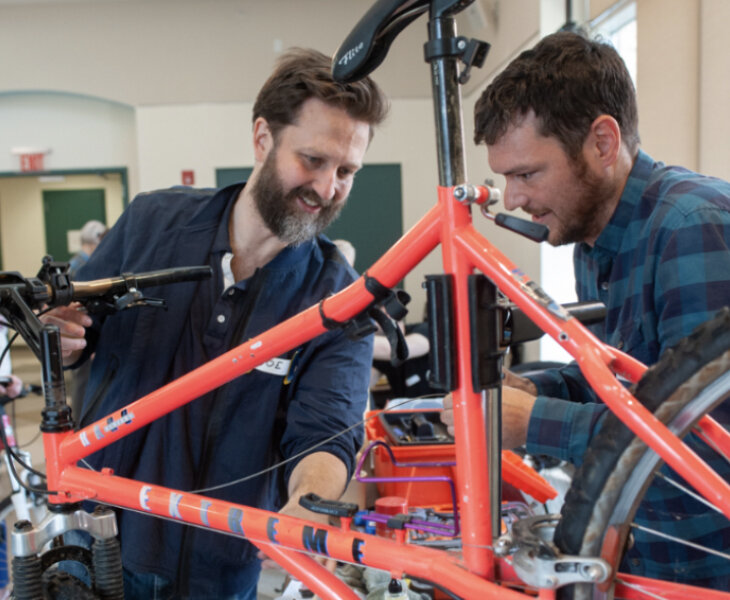 Photo of two peole repairing a bicycle.