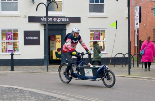 Photo of a person riding a cargo bike in a small downtown commercial street.