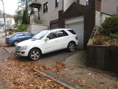 2 cars parked partially in driveways and partly across the sidewalk, both in front of garage doors.